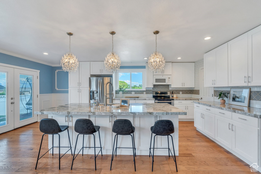 Kitchen with stainless steel appliances, a chandelier, crown molding, white cabinets, and french doors