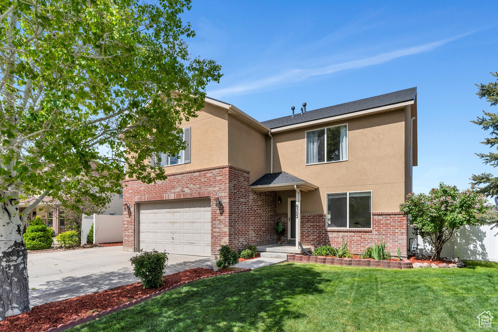 View of front facade featuring stucco siding, a garage, driveway, and brick siding