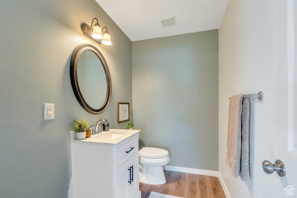 Half bathroom featuring wood finished floors, toilet, baseboards, and vanity