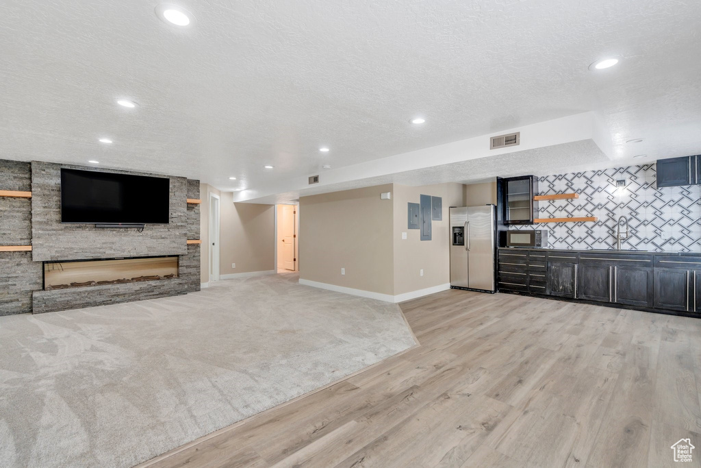 Unfurnished living room with light wood-type flooring, recessed lighting, a stone fireplace, baseboards, and a textured ceiling