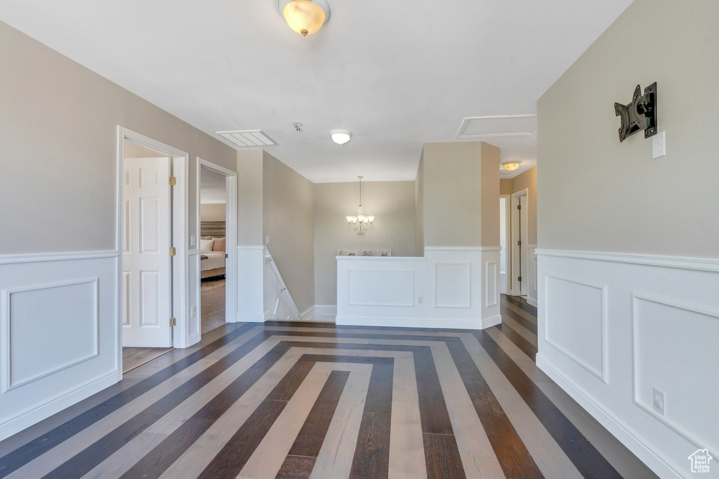 Unfurnished room featuring dark wood-style floors, a wainscoted wall, a chandelier, and a decorative wall