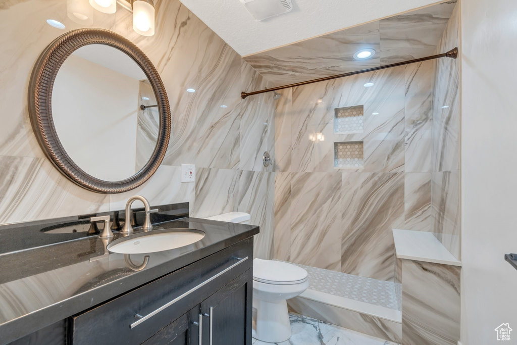 Full bathroom with tile walls, toilet, a marble finish shower, and vanity