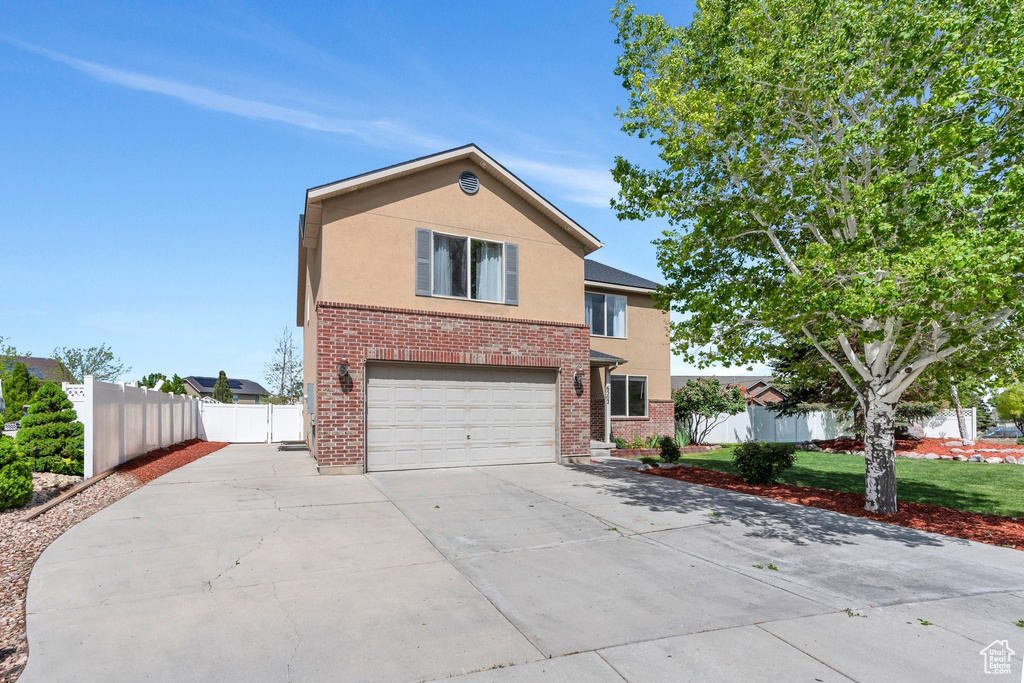 Traditional home featuring stucco siding, a garage, concrete driveway, fence, and brick siding