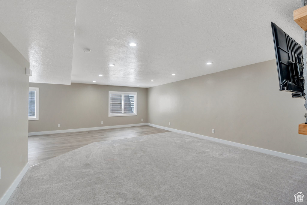 Unfurnished living room with light colored carpet, a textured ceiling, recessed lighting, and baseboards