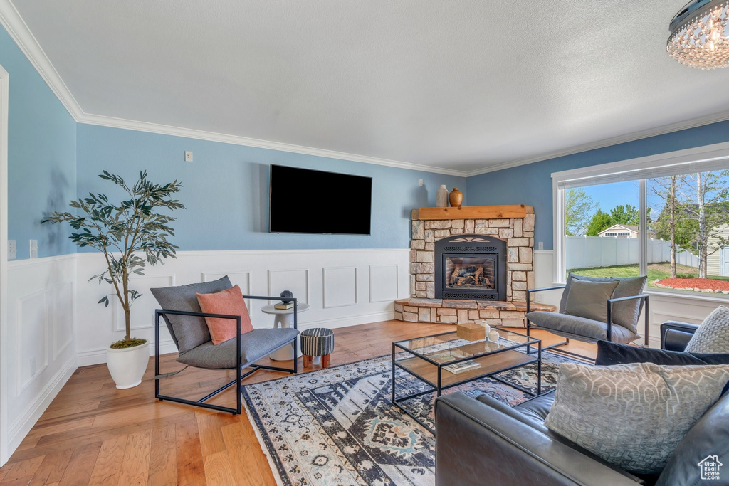 Living room featuring wood-type flooring, a fireplace, wainscoting, ornamental molding, and a chandelier