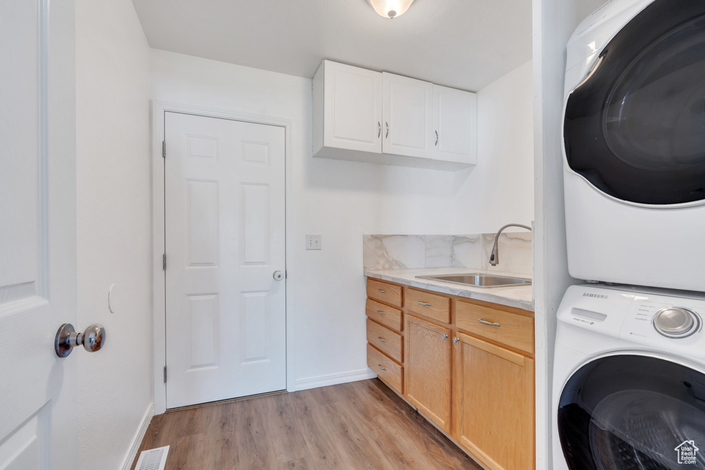 Laundry area featuring stacked washer and clothes dryer, light wood-type flooring, baseboards, and cabinet space