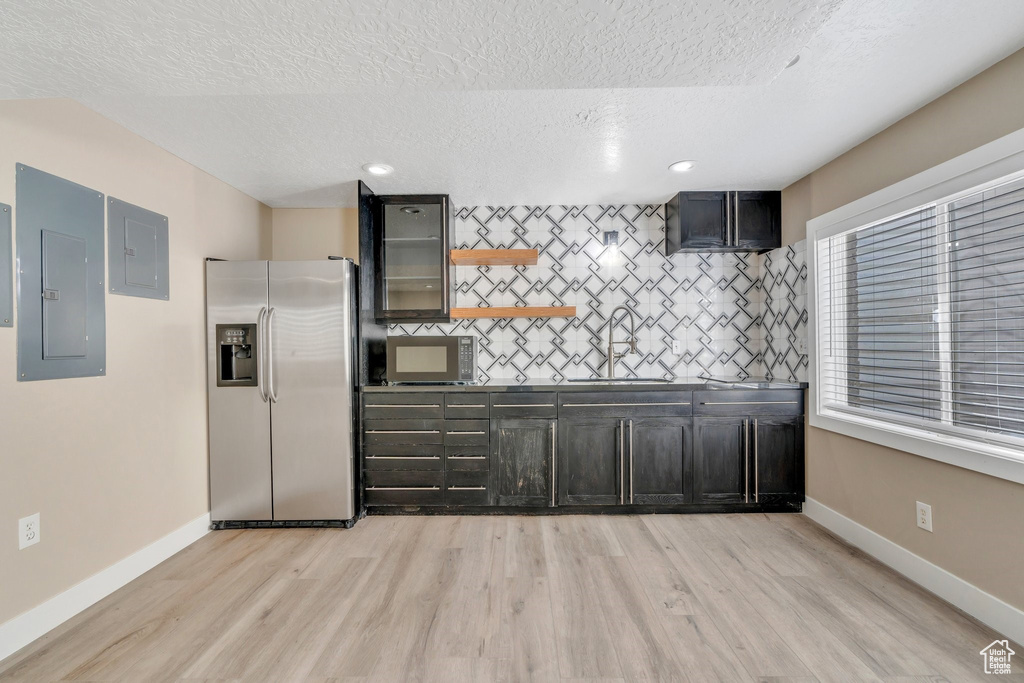 Kitchen with appliances with stainless steel finishes, a sink, a textured ceiling, light wood-style flooring, and electric panel