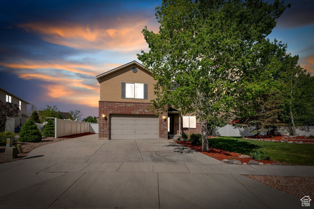 View of front of property with driveway, brick siding, a garage, and stucco siding