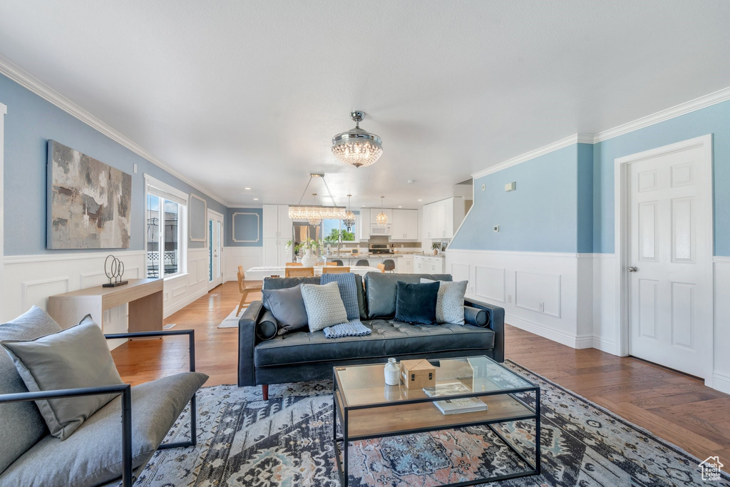 Living room with a chandelier, crown molding, wainscoting, a decorative wall, and plenty of natural light