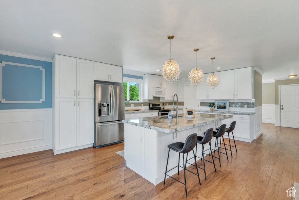 Kitchen with appliances with stainless steel finishes, ornamental molding, a breakfast bar area, a chandelier, and light wood-style floors