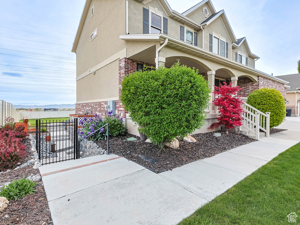View of property exterior with covered porch, fence, a gate, stucco siding, and brick siding