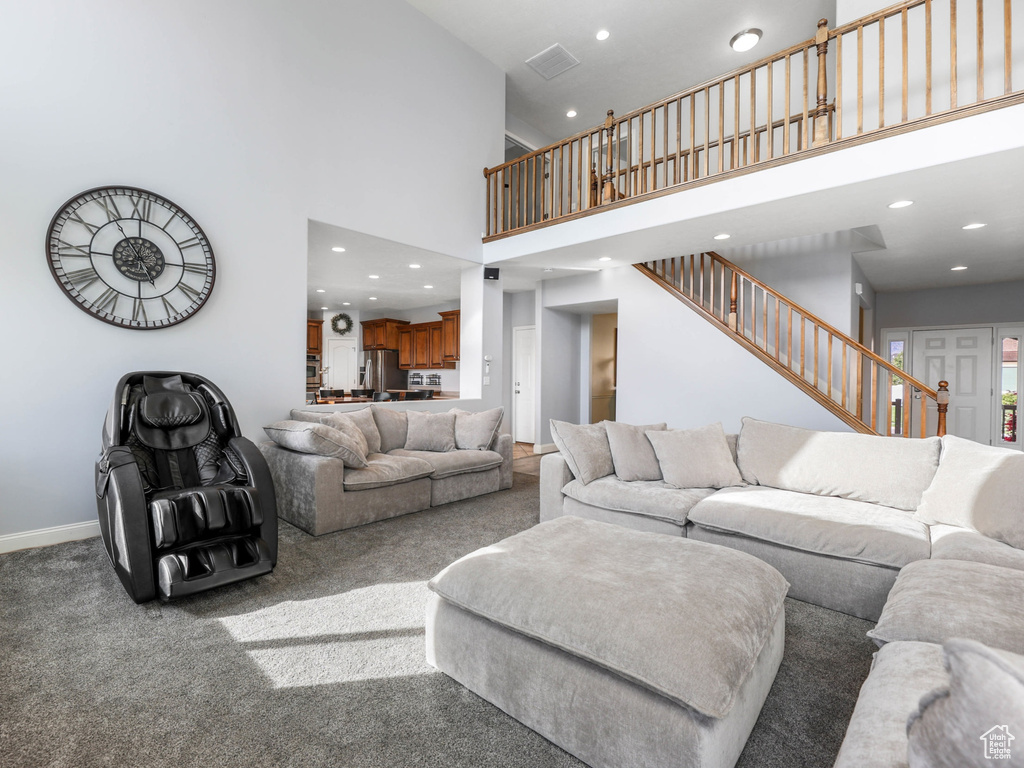 Carpeted living area with stairs, recessed lighting, baseboards, and a towering ceiling