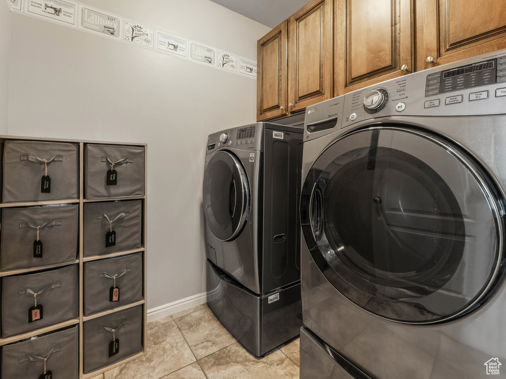 Laundry room featuring washer and clothes dryer, cabinet space, baseboards, and light tile patterned floors