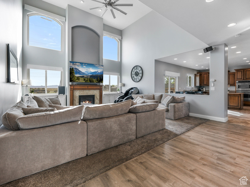 Living room with a towering ceiling, light wood-type flooring, ceiling fan, a lit fireplace, and recessed lighting