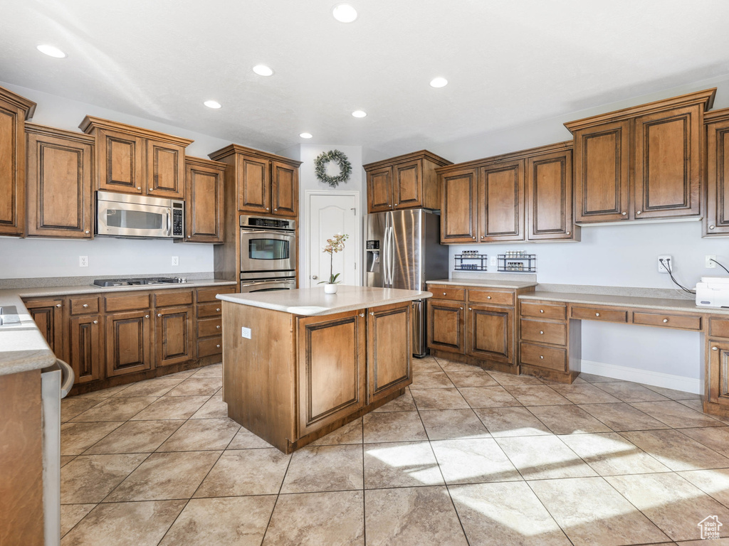 Kitchen featuring appliances with stainless steel finishes, recessed lighting, brown cabinets, a center island, and light countertops