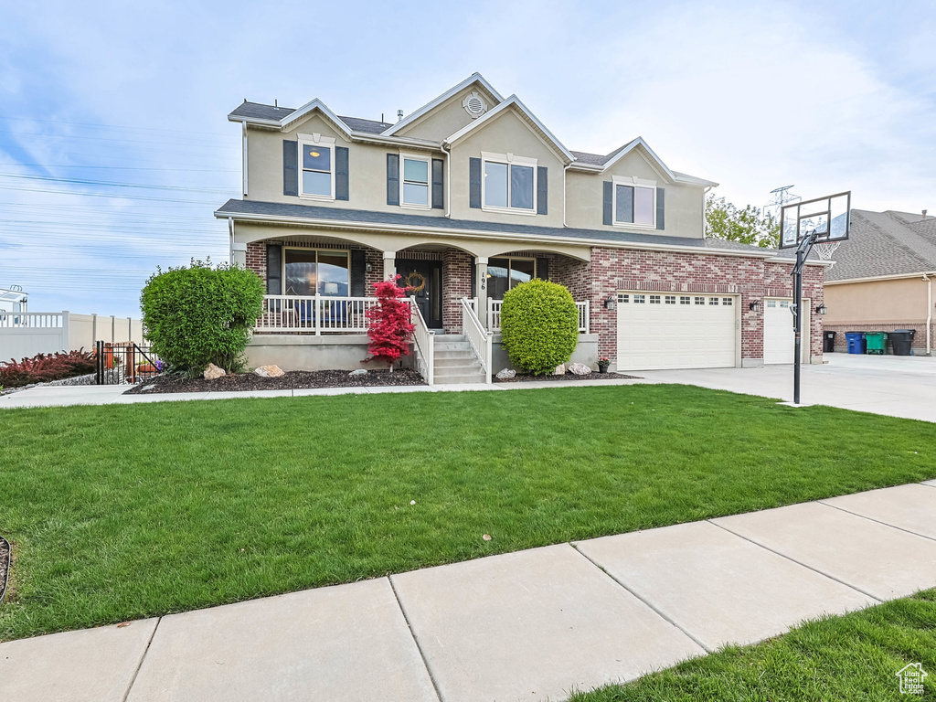 View of front facade with a porch, stucco siding, a front lawn, concrete driveway, and an attached garage