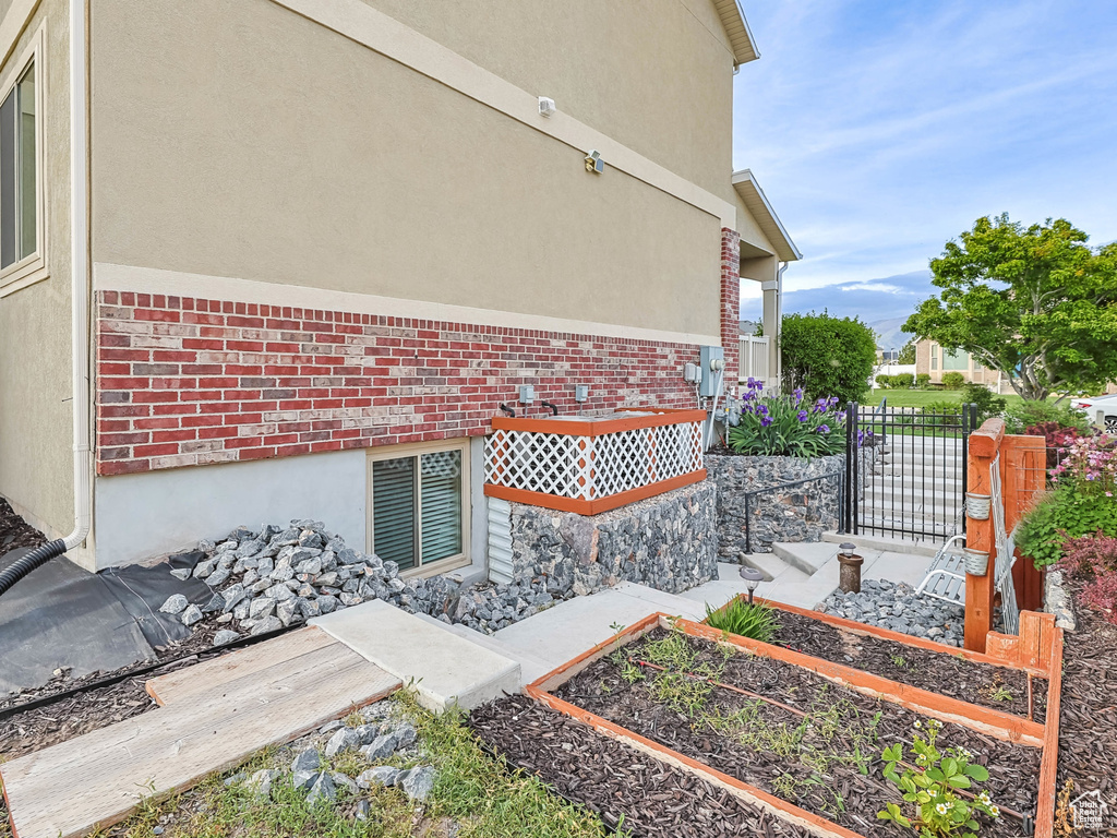View of side of property featuring a garden, brick siding, and stucco siding