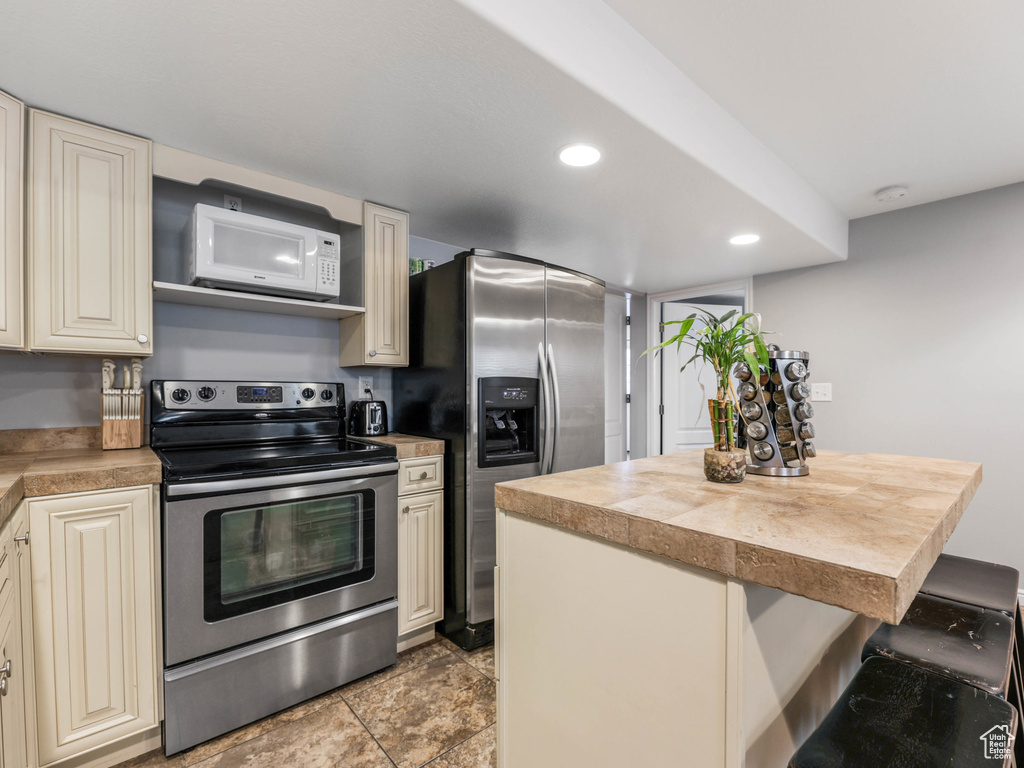 Kitchen with stainless steel appliances, cream cabinets, light countertops, a kitchen breakfast bar, and a kitchen island