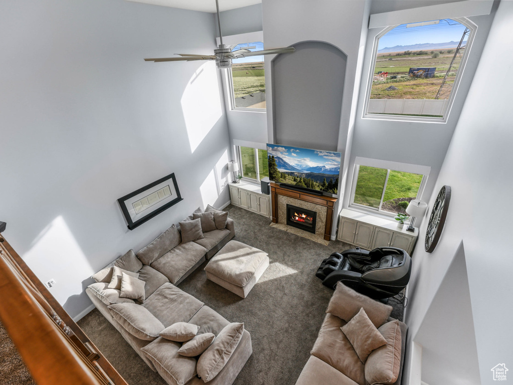 Carpeted living area featuring a high ceiling, ceiling fan, and a high end fireplace