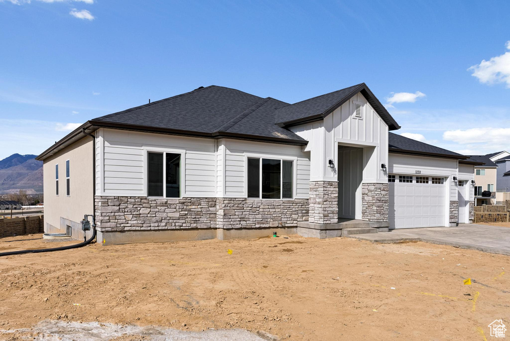 View of front facade with an attached garage, stone siding, a shingled roof, board and batten siding, and driveway