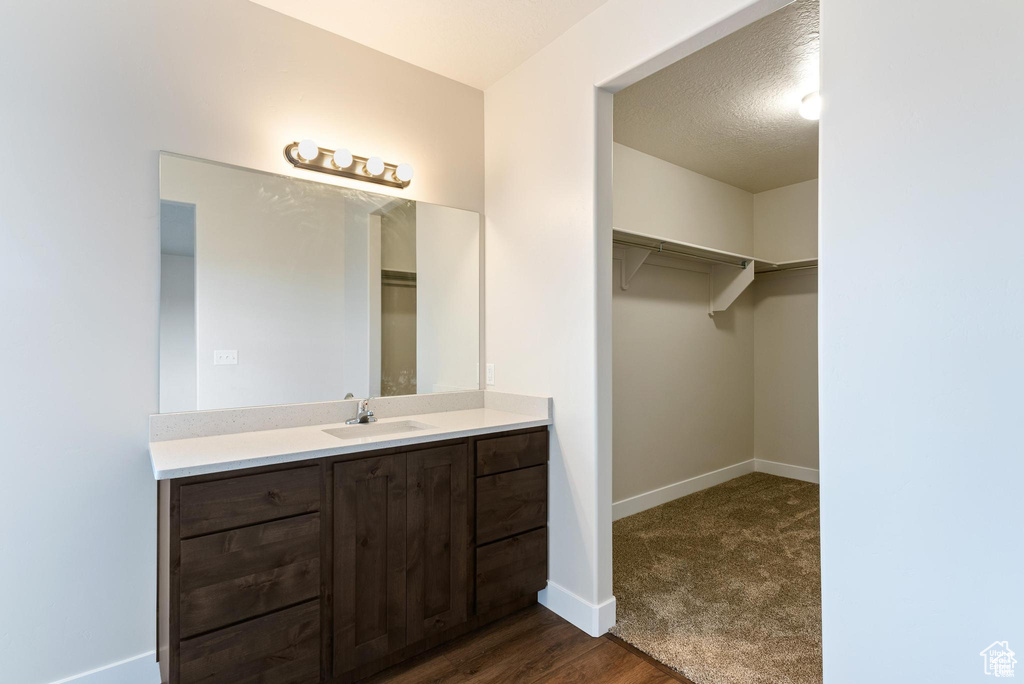 Bathroom with baseboards, vanity, wood finished floors, a spacious closet, and a textured ceiling