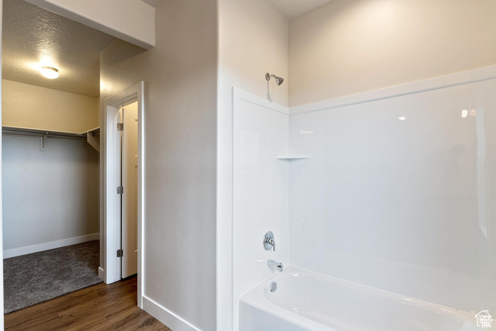 Full bathroom with wood finished floors, tub / shower combination, baseboards, and a spacious closet