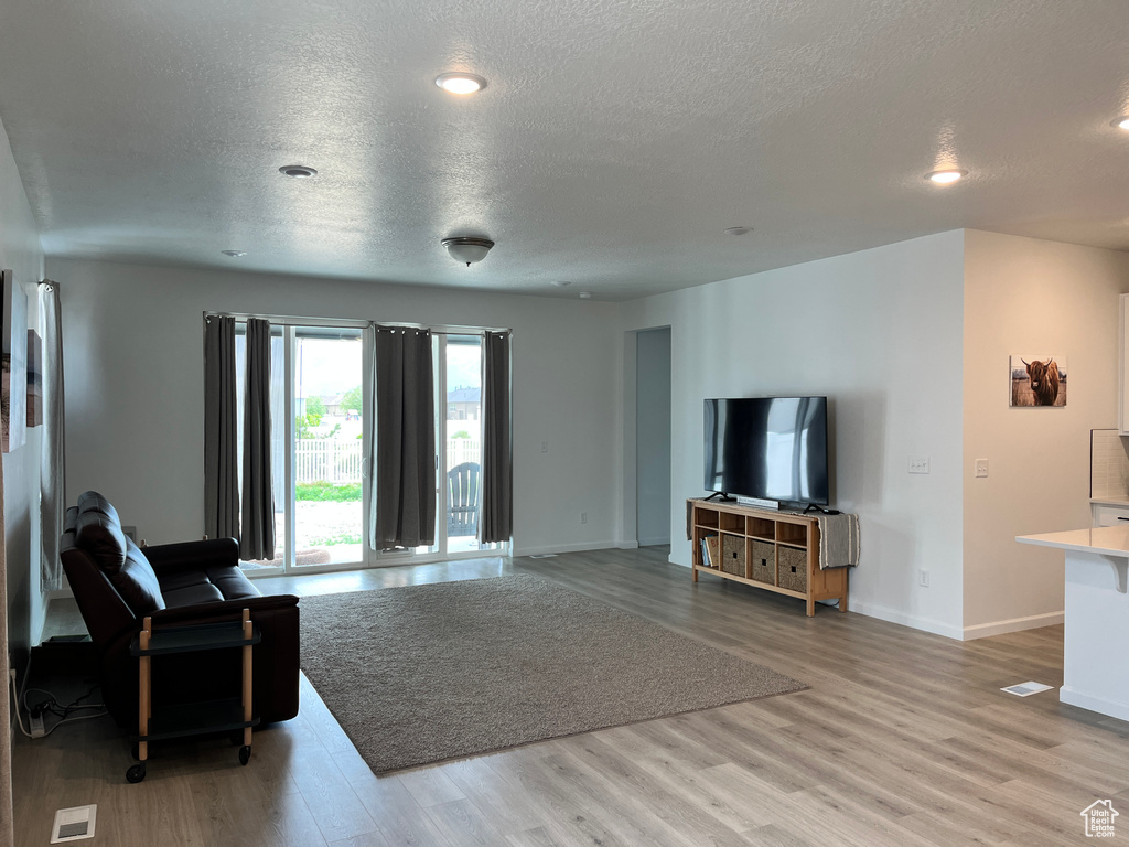 Living area with a textured ceiling, light wood finished floors, baseboards, and recessed lighting
