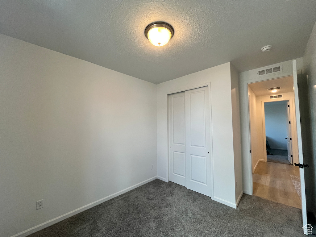 Unfurnished bedroom featuring a closet, dark colored carpet, a textured ceiling, and baseboards