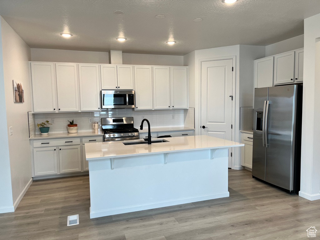 Kitchen with appliances with stainless steel finishes, a sink, white cabinets, and recessed lighting