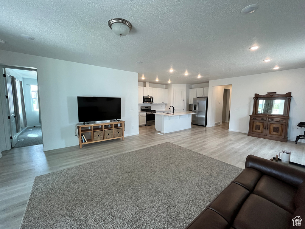 Living area with light wood-style floors, a textured ceiling, and recessed lighting