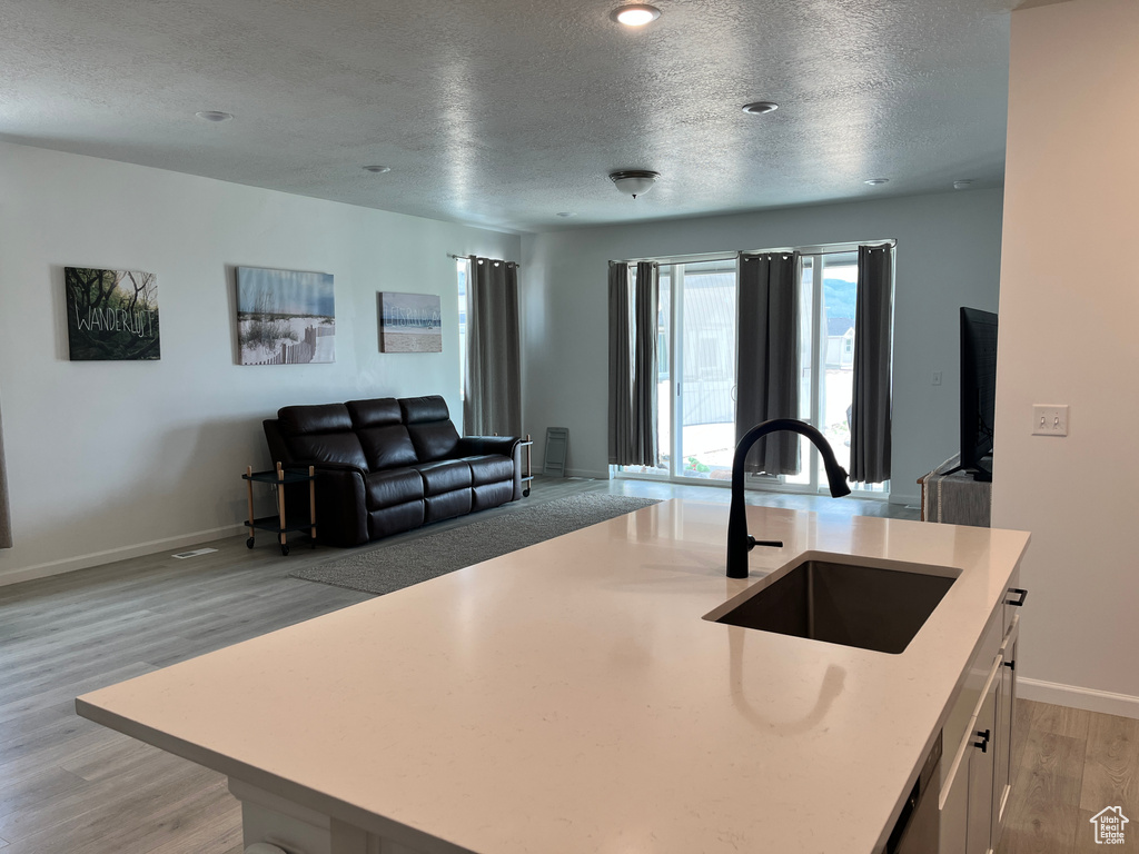 Kitchen with a sink, light countertops, a textured ceiling, open floor plan, and light wood finished floors
