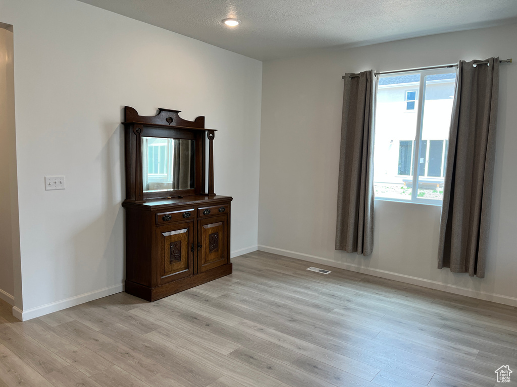 Unfurnished living room with light wood-style floors, baseboards, and a textured ceiling