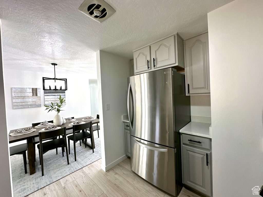 Kitchen with freestanding refrigerator, light wood finished floors, a chandelier, light countertops, and a textured ceiling