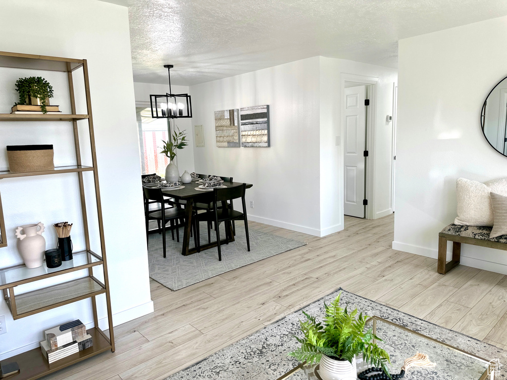 Dining space with a chandelier, light wood-type flooring, baseboards, and a textured ceiling