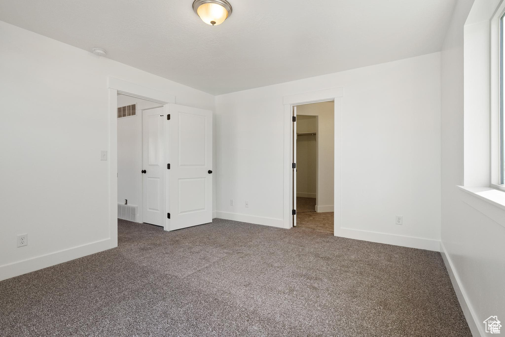 Unfurnished bedroom featuring carpet floors, baseboards, a walk in closet, and a closet