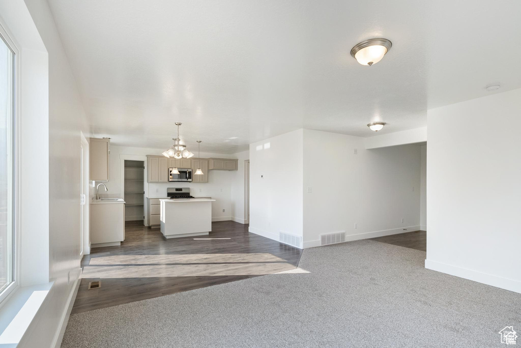Unfurnished living room with a chandelier, a sink, baseboards, and dark carpet