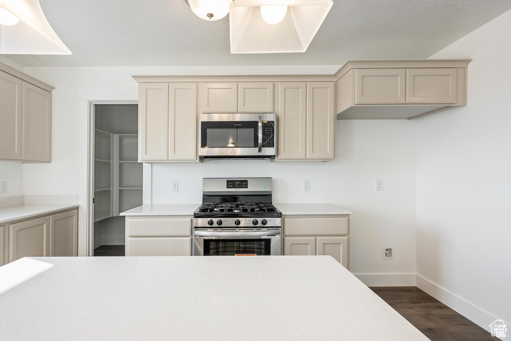 Kitchen featuring stainless steel appliances, baseboards, dark wood finished floors, light countertops, and cream cabinets