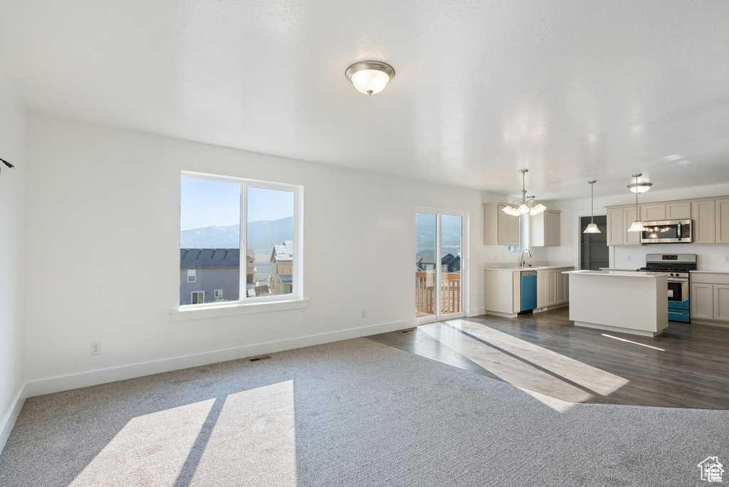Unfurnished living room with plenty of natural light, dark colored carpet, baseboards, and a chandelier