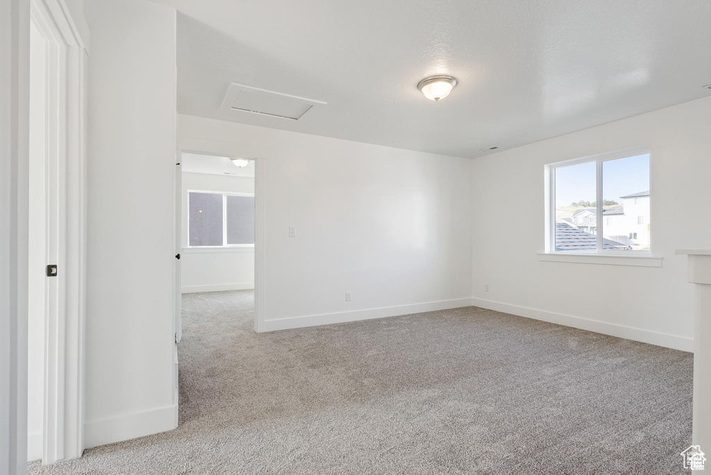 Carpeted empty room featuring attic access and baseboards