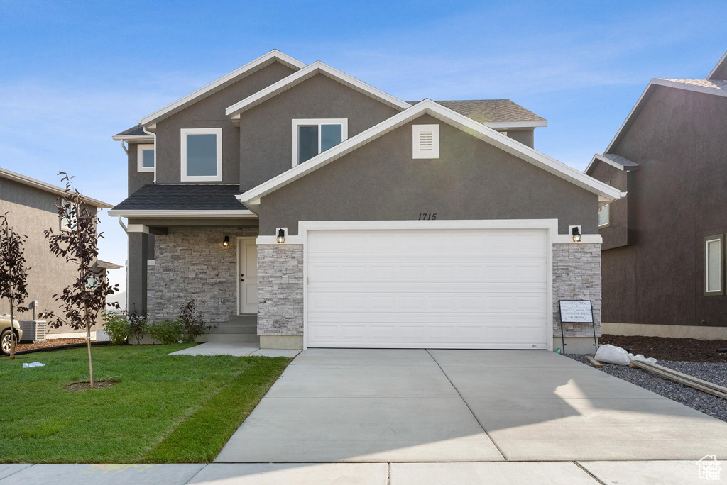 View of front facade with stone siding, driveway, a front yard, and stucco siding
