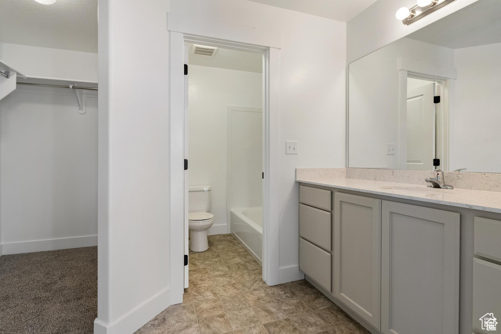 Bathroom featuring toilet, vanity, a spacious closet, and baseboards