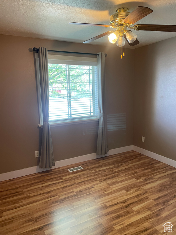 Unfurnished room featuring a ceiling fan, wood finished floors, a textured ceiling, and baseboards
