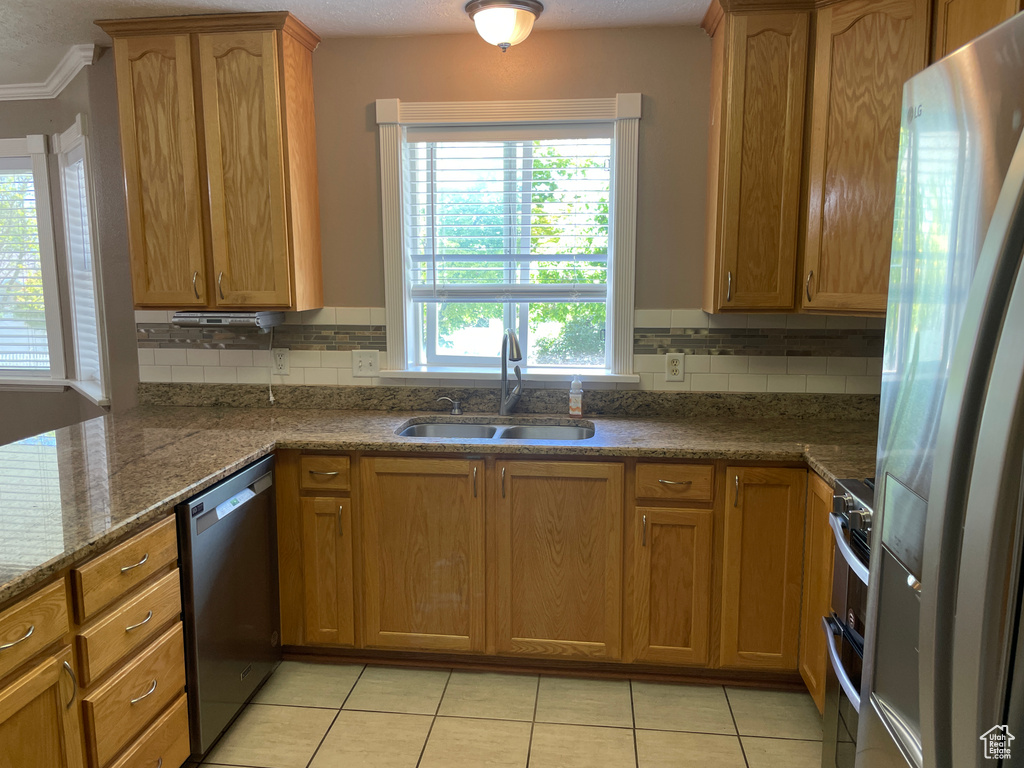 Kitchen featuring appliances with stainless steel finishes, a sink, tasteful backsplash, light tile patterned flooring, and ornamental molding