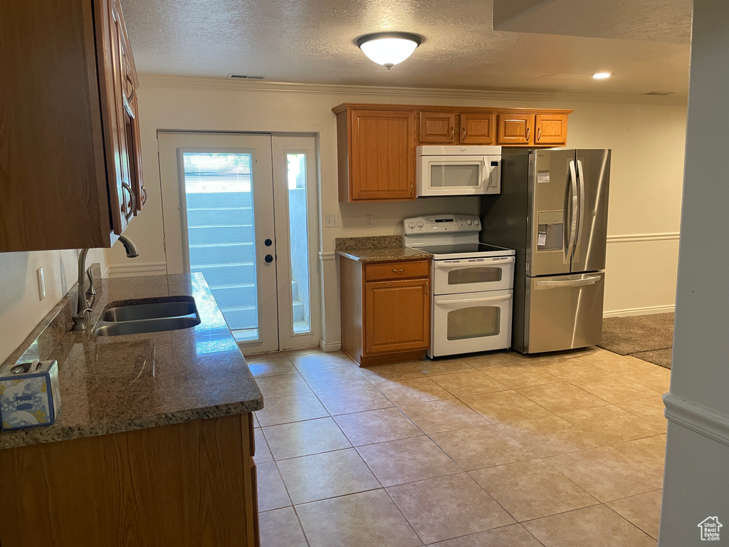 Kitchen with white appliances, a sink, crown molding, a textured ceiling, and dark stone countertops