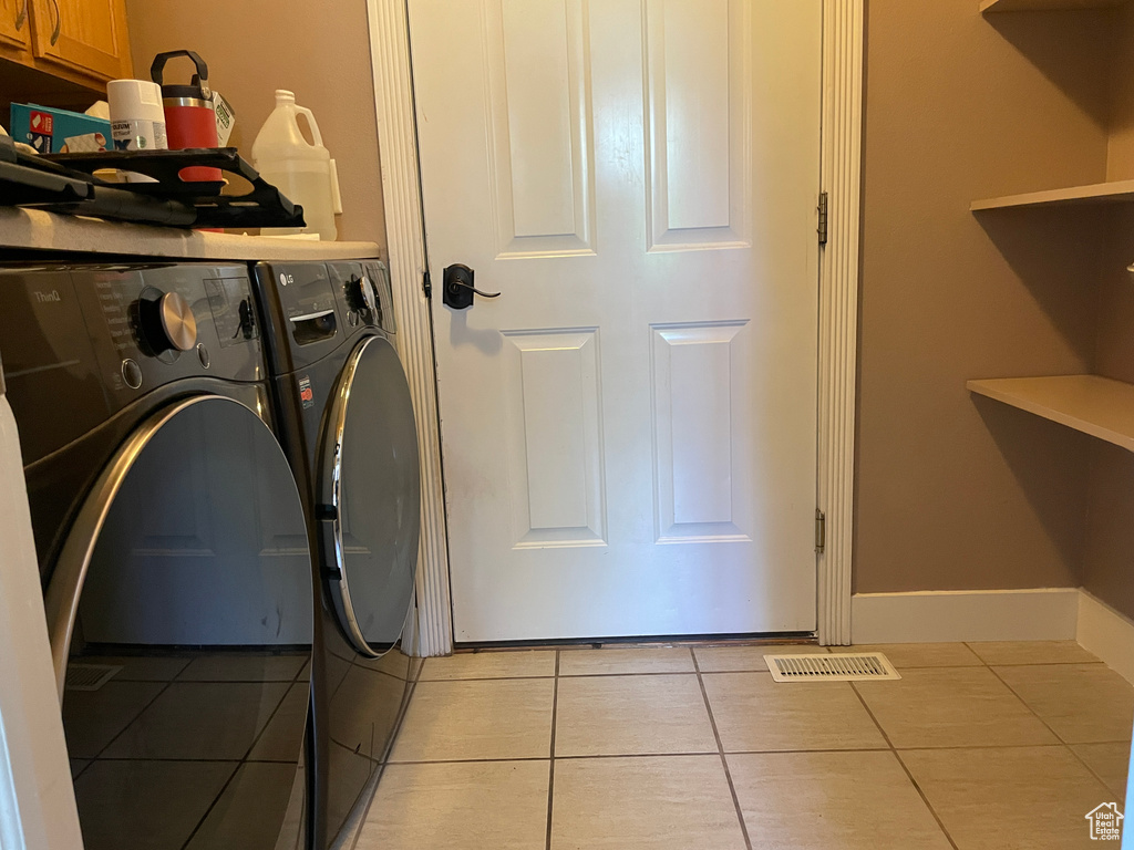 Laundry area with independent washer and dryer, light tile patterned floors, and cabinet space