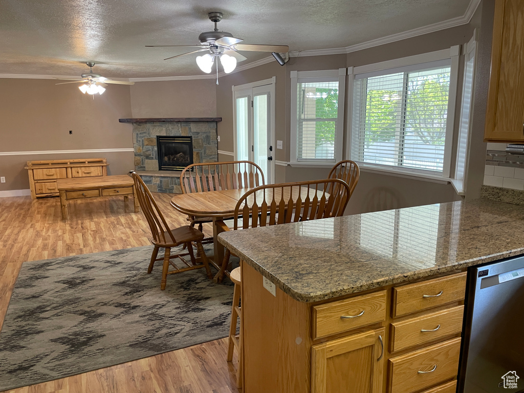 Kitchen with stainless steel dishwasher, a ceiling fan, wood finished floors, crown molding, and a stone fireplace