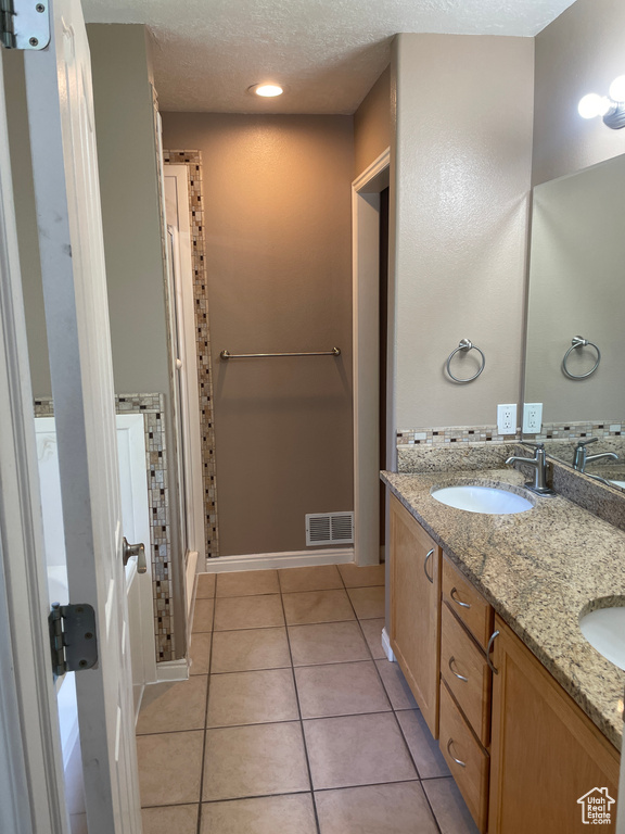 Full bathroom featuring tile patterned flooring, double vanity, and a textured ceiling