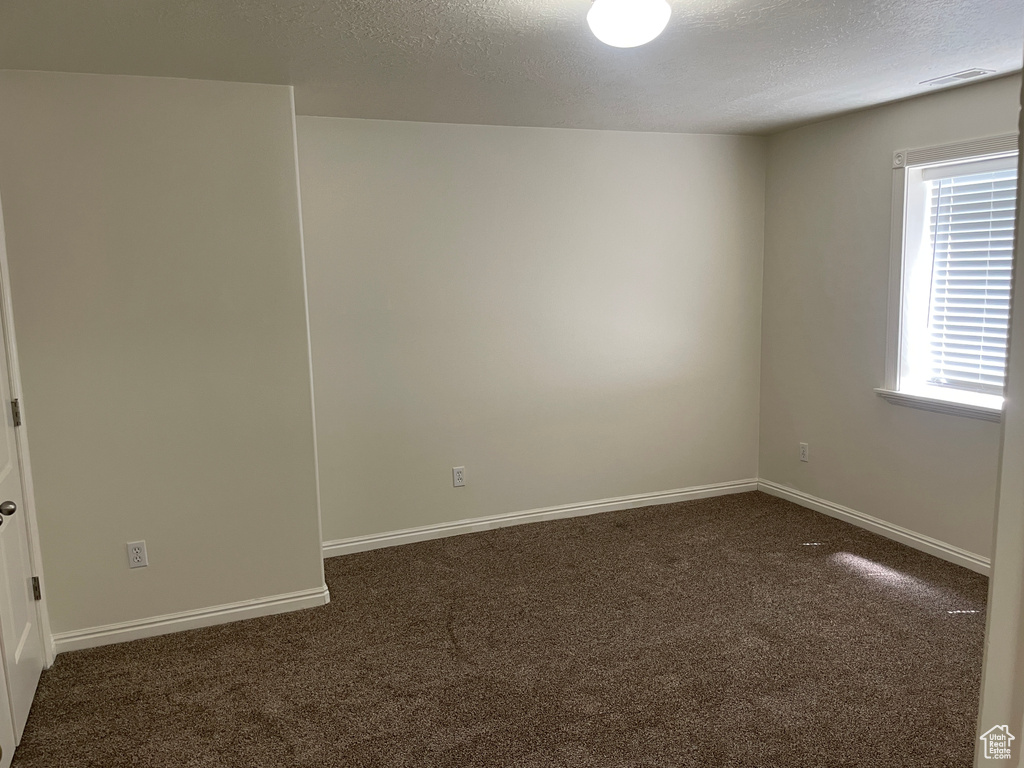 Spare room with dark colored carpet, a textured ceiling, and baseboards