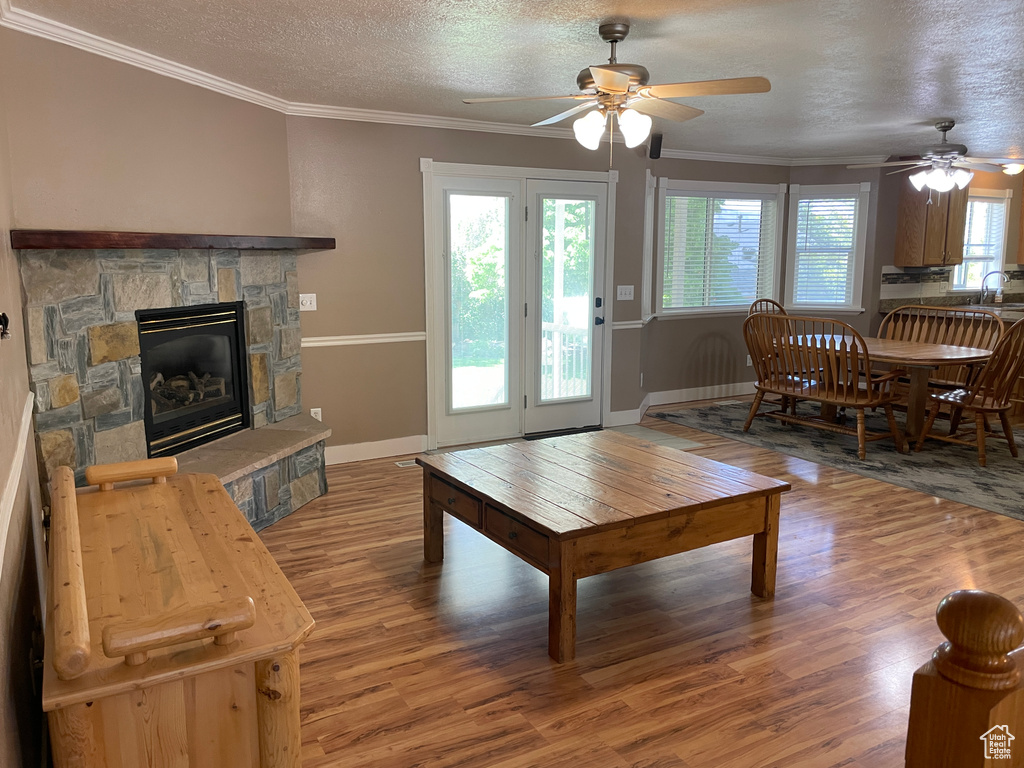 Living area with ceiling fan, light wood finished floors, baseboards, a fireplace, and a textured ceiling
