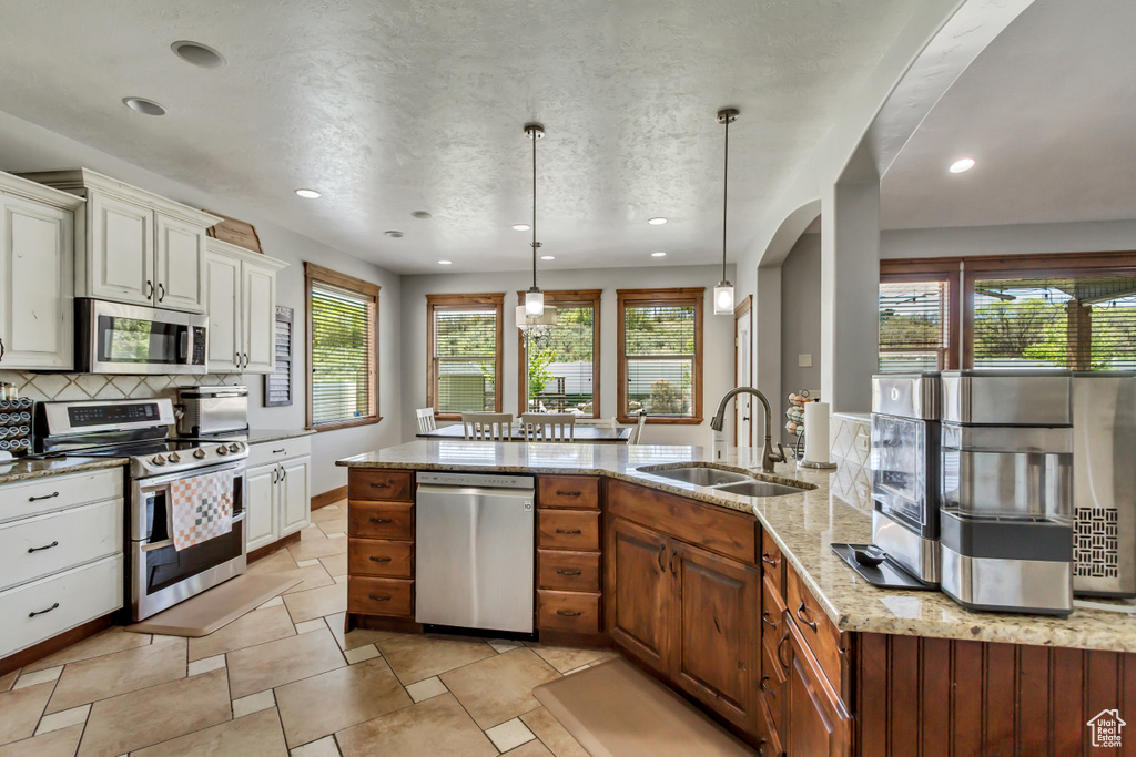 Kitchen with stainless steel appliances, a sink, backsplash, light stone countertops, and plenty of natural light